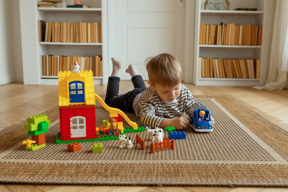 Niño construyendo con bloques encajables de colores tumbado en la alfombra.