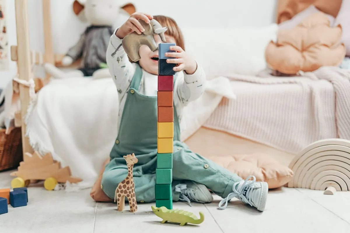 Niña pequeña construyendo una torre alta de bloques de colores junto a animales de madera.