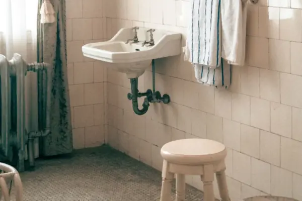 Baño luminoso con lavabo antiguo, toallas colgadas y un taburete bajo de madera