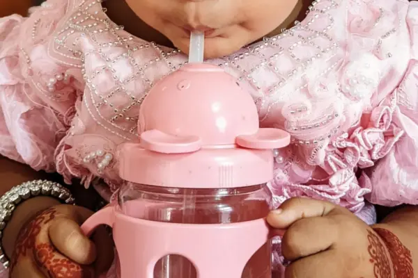 Bebé sujetando con las dos manos un vaso de aprendizaje rosa con asas y bebiendo por su boquilla de pajita