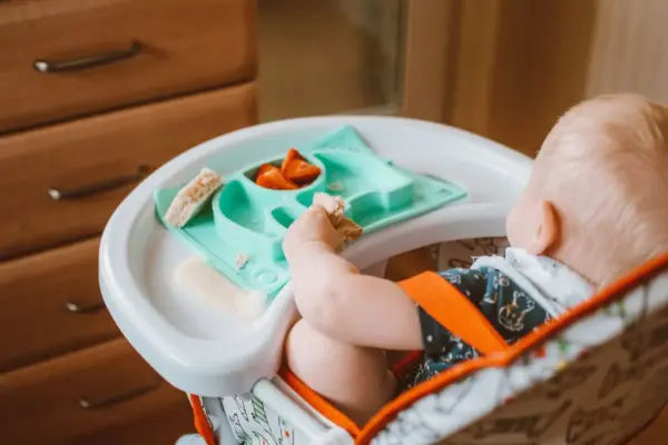 Bebé comiendo fruta y pan en la bandeja de su trona