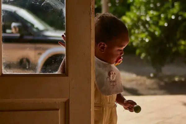 Bebé con babero de tela junto a una puerta soleada