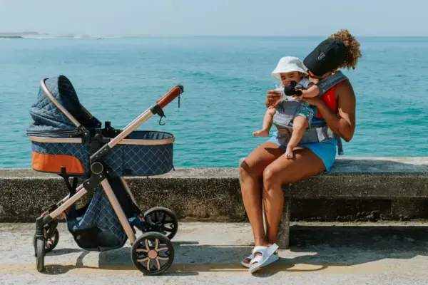Cochecito de bebé con capazo junto a una madre en un paseo marítimo