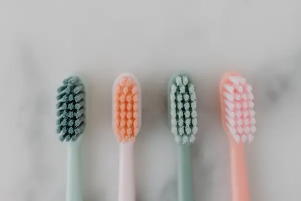 Primer plano de las cerdas de cuatro cepillos de dientes de colores pastel sobre una encimera de mármol claro