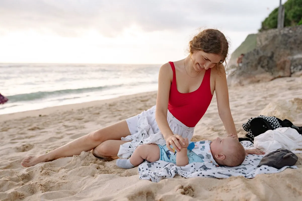 Una madre y su bebé se miran a los ojos sentados en la playa al atardecer.