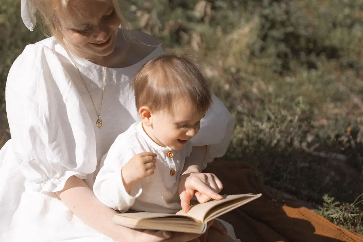 Madre y su hijo pequeño leyendo un cuento al aire libre, señalando la página.