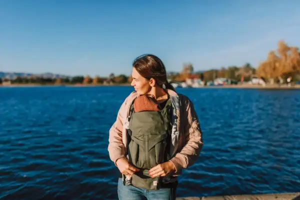 Madre porteando a su bebé en un portabebés junto al agua