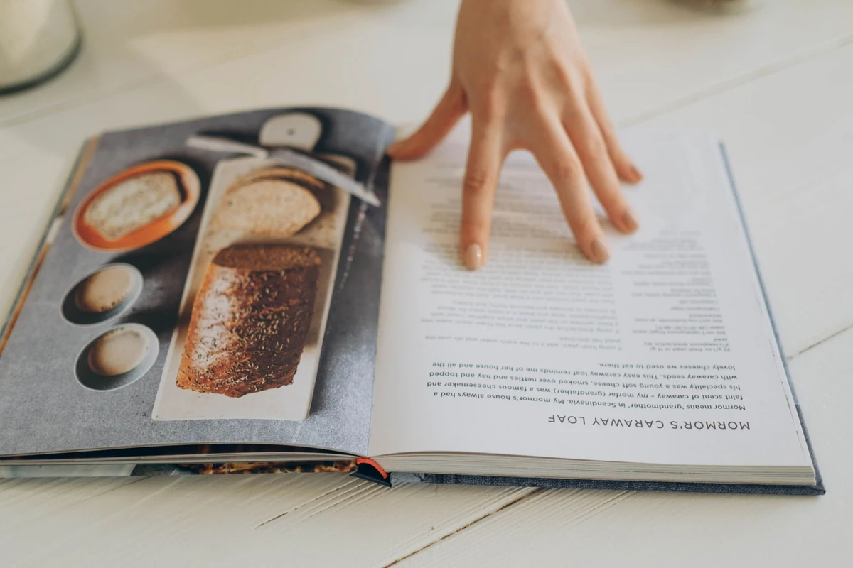 Libro de recetas abierto sobre la mesa con una mano sujetando la página