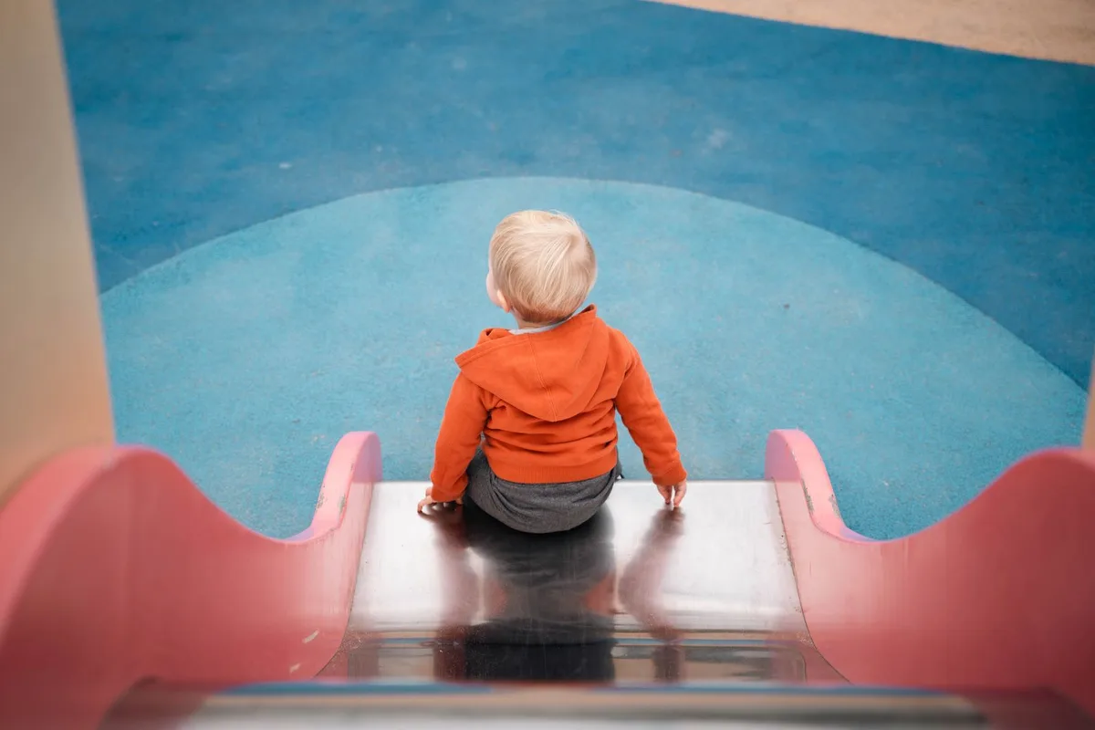 Niño pequeño sentado en lo alto de un tobogán del parque, a punto de deslizarse.
