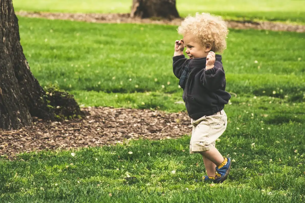 Niño pequeño de unos 3 años corriendo por el césped de un parque, un ejemplo de motricidad gruesa en acción.