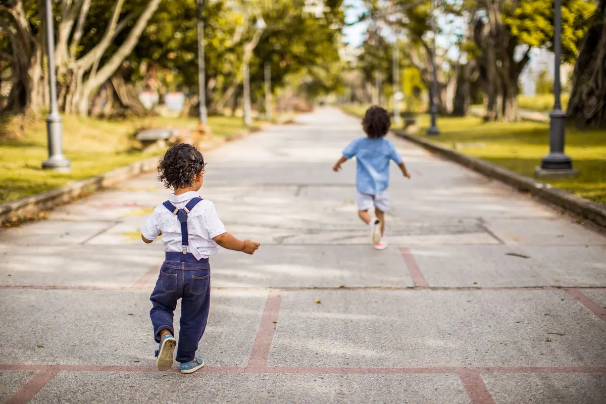 Dos niños pequeños corriendo por el paseo de un parque arbolado.