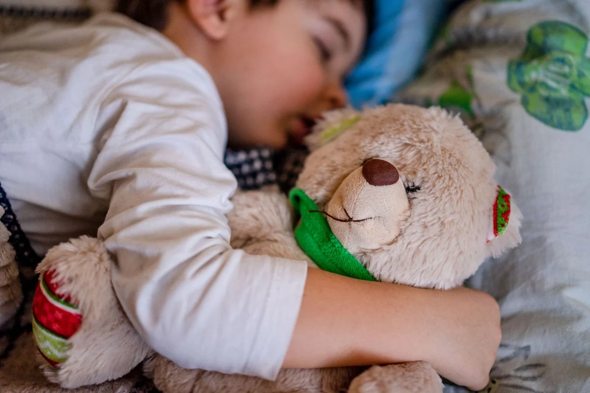 Niño pequeño durmiendo tranquilo abrazado a un peluche, sin chupete