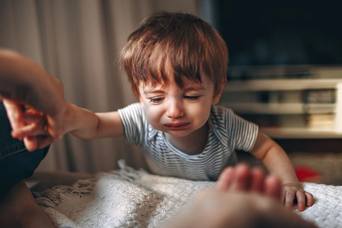 Niño de unos dos años llorando y tendiendo la mano en casa