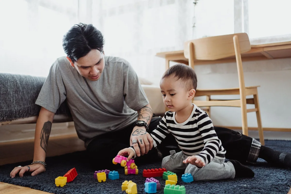 Padre y niño pequeño jugando con bloques de colores sentados en el suelo del salón.