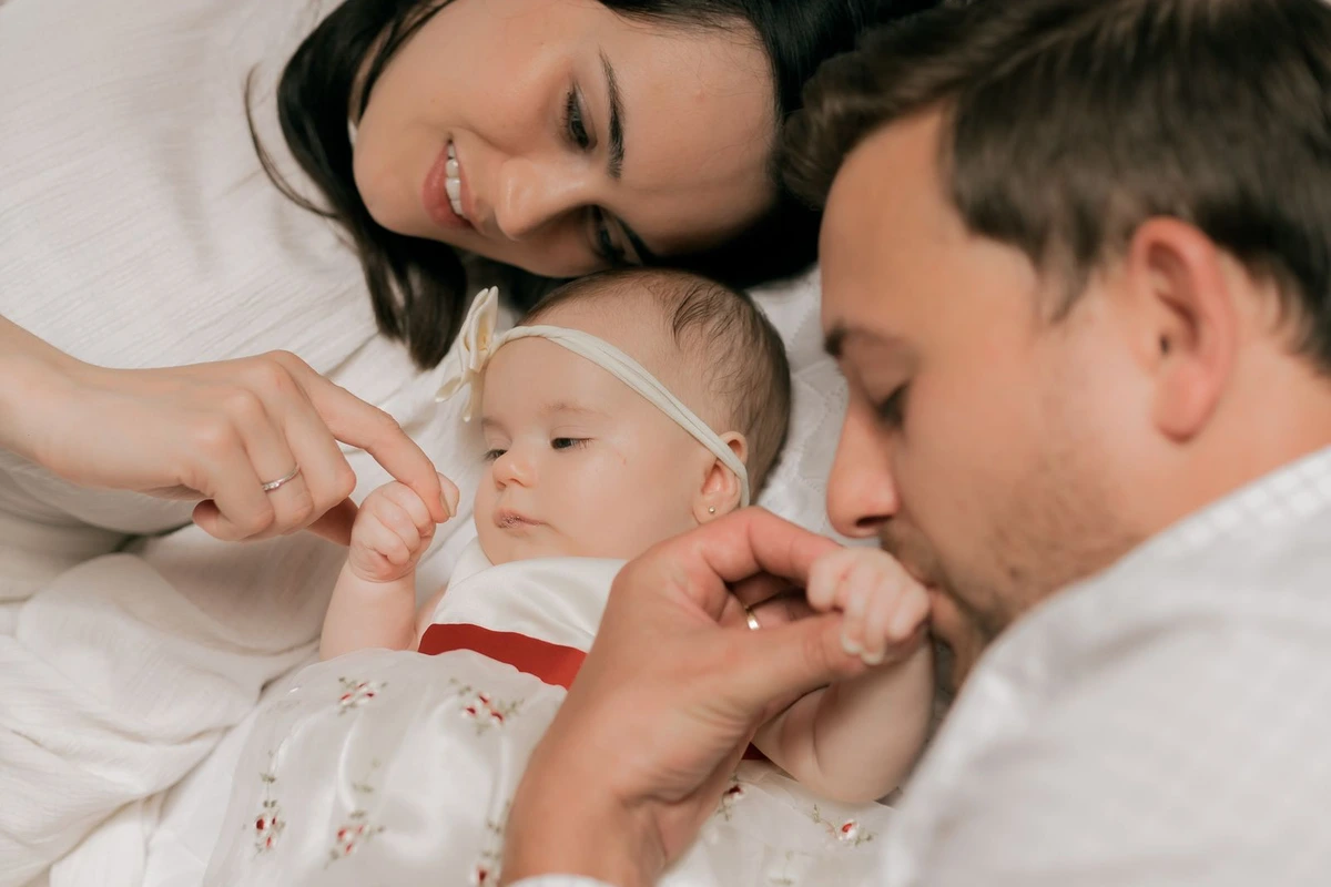 Madre y padre tumbados junto a su bebé acariciándolo con ternura en la cama.