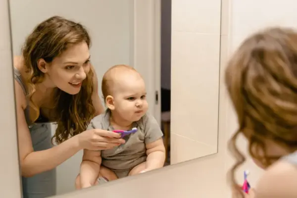 Madre cepillando los dientes a su bebé frente al espejo