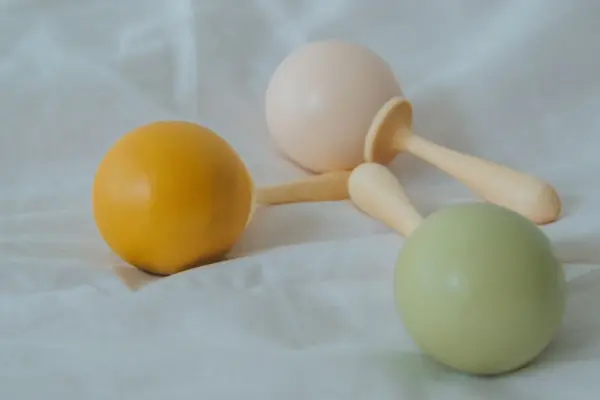 Tres sonajeros de madera para bebés en tonos pastel apoyados sobre una tela clara