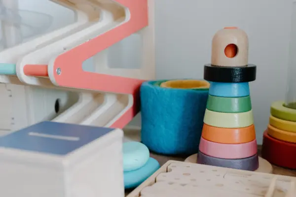 Torre de aros apilables de colores y vasos encajables de fieltro junto a otros juguetes de madera para bebés en un cuarto infantil